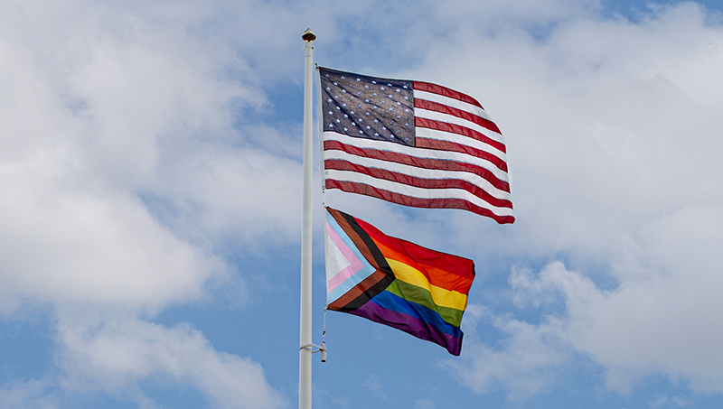 一个美国国旗和一个同性恋群体+国旗挥舞着旗杆。