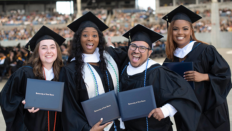 四名毕业生，戴着帽子，穿着长袍，摆姿势拍照。